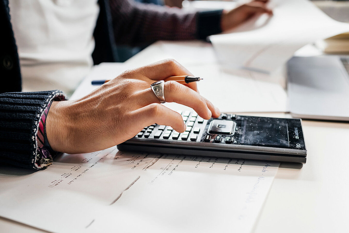 Studienfinanzierung Die Hand eines Mannes hält einen Stift und tippt auf einem Taschenrechner