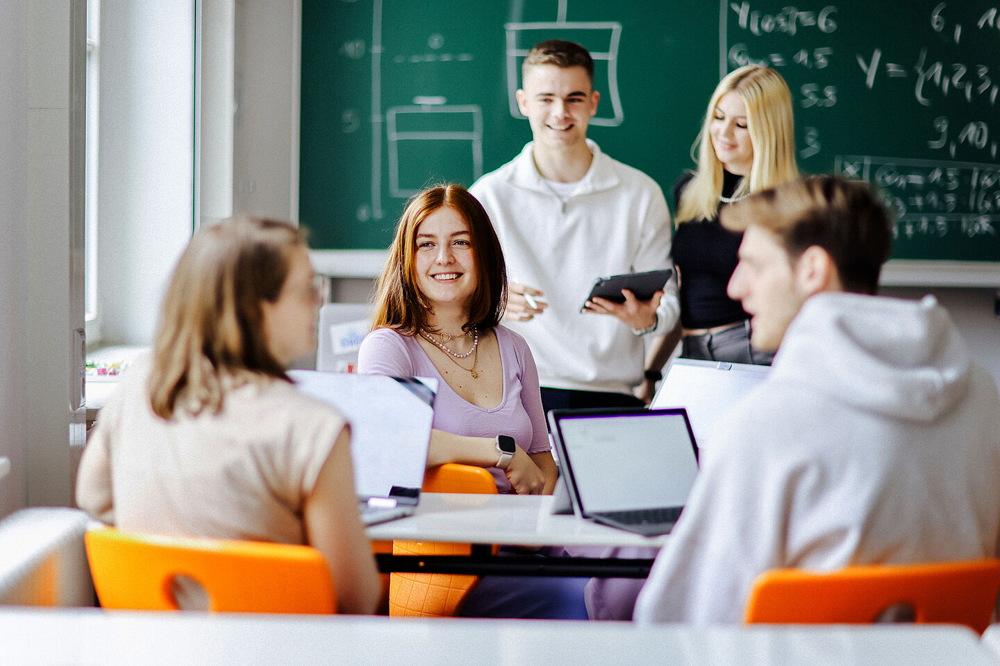 Fünf Studierende im Seminarraum mit Laptops und an der Tafel ein Tafelbild zu Statistik